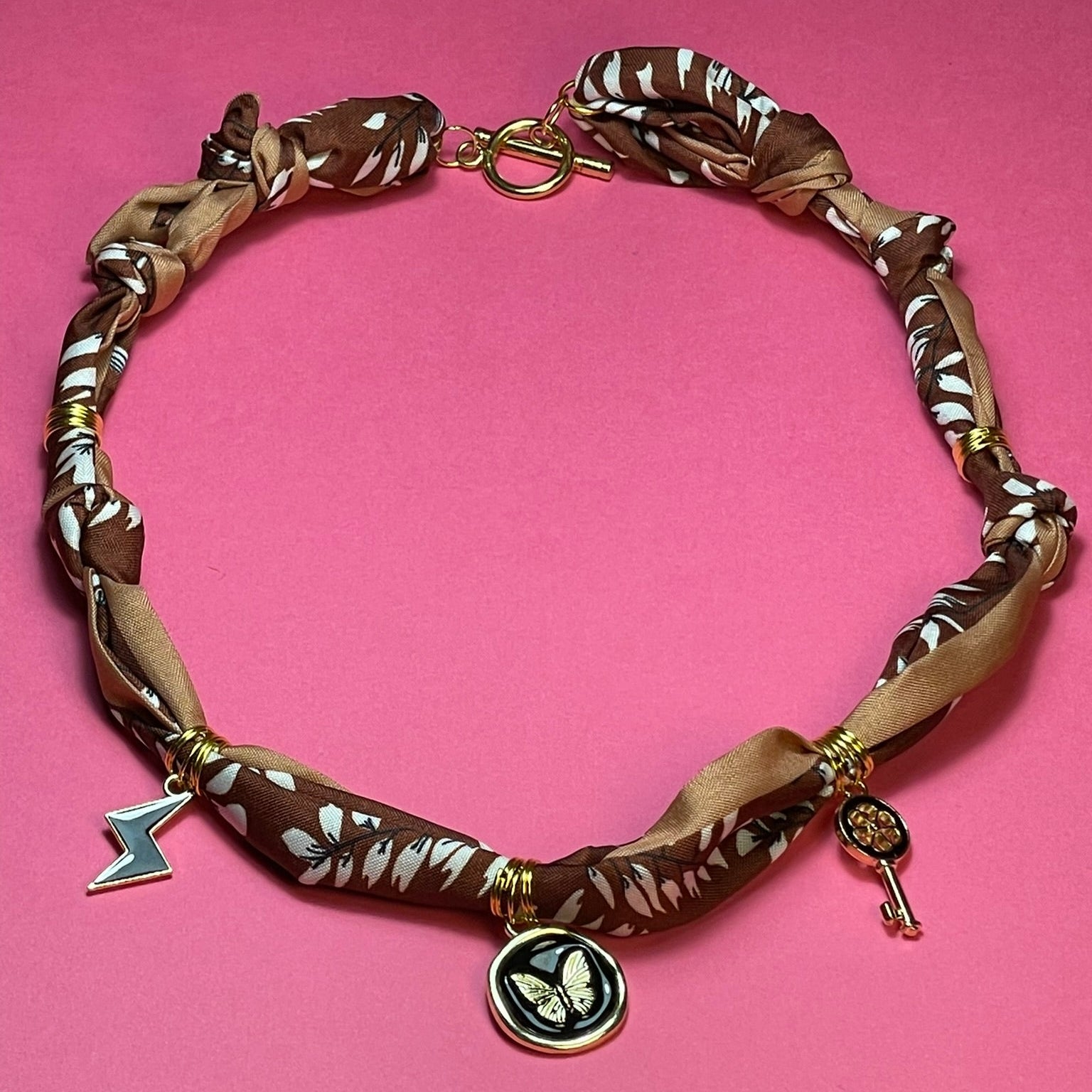 Collar artesanal con dije dorado y pañuelo trenzado, diseño bohemio hecho a mano por Hilma.