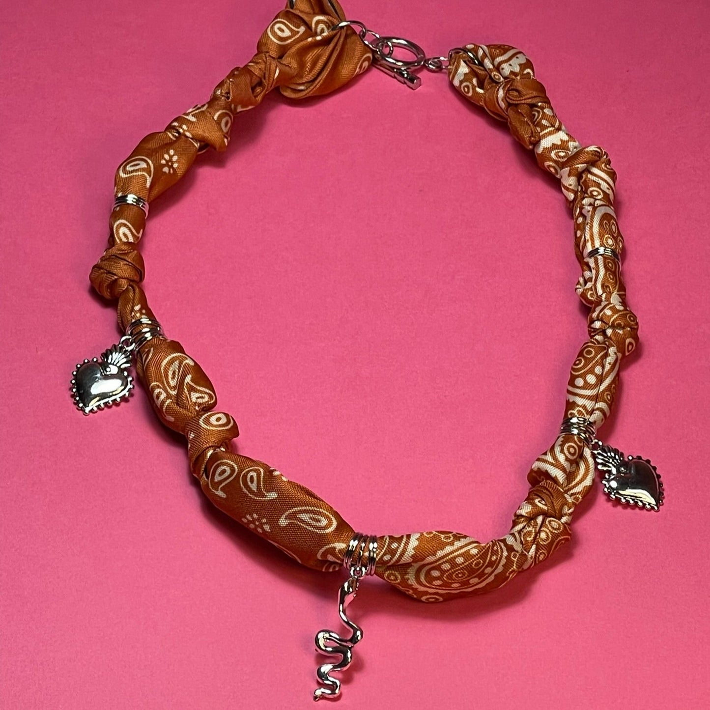 Collar artesanal con dije dorado y pañuelo trenzado, diseño bohemio hecho a mano por Hilma.