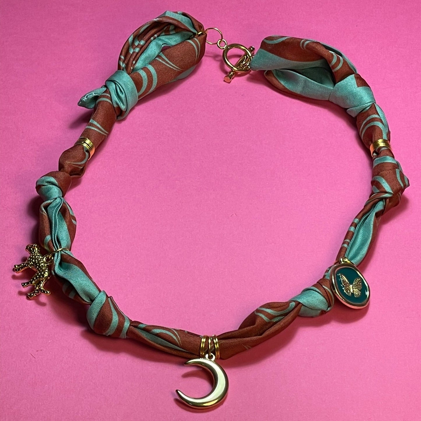 Collar artesanal con dije dorado y pañuelo trenzado, diseño bohemio hecho a mano por Hilma.